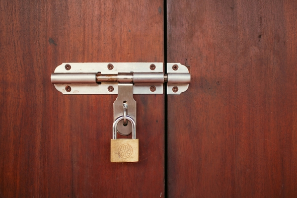 A wooden door held shut with a bolt and padlock